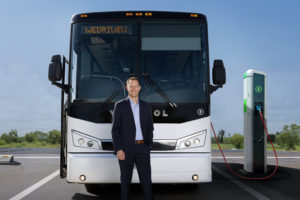 A man in a suit stands in front of a bus displaying "WeDriveU" as the destination